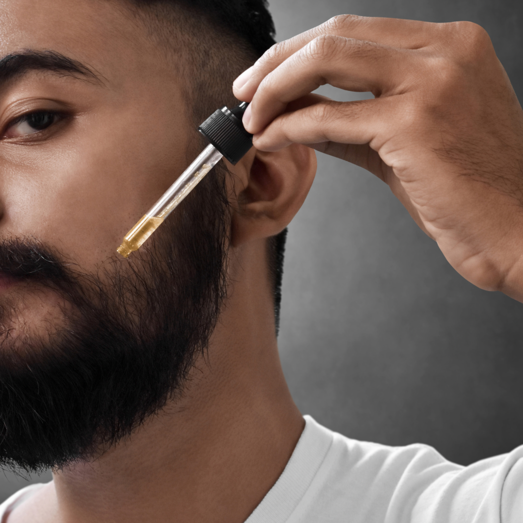 A man carefully dropping beard oil onto his face, demonstrating a precise and thoughtful grooming routine.