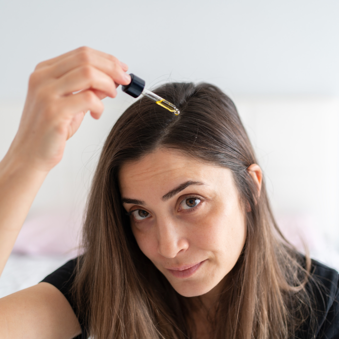 A woman is shown applying hair oil to her scalp, exemplifying a self-care hair care regimen focused on nourishment and hydration.